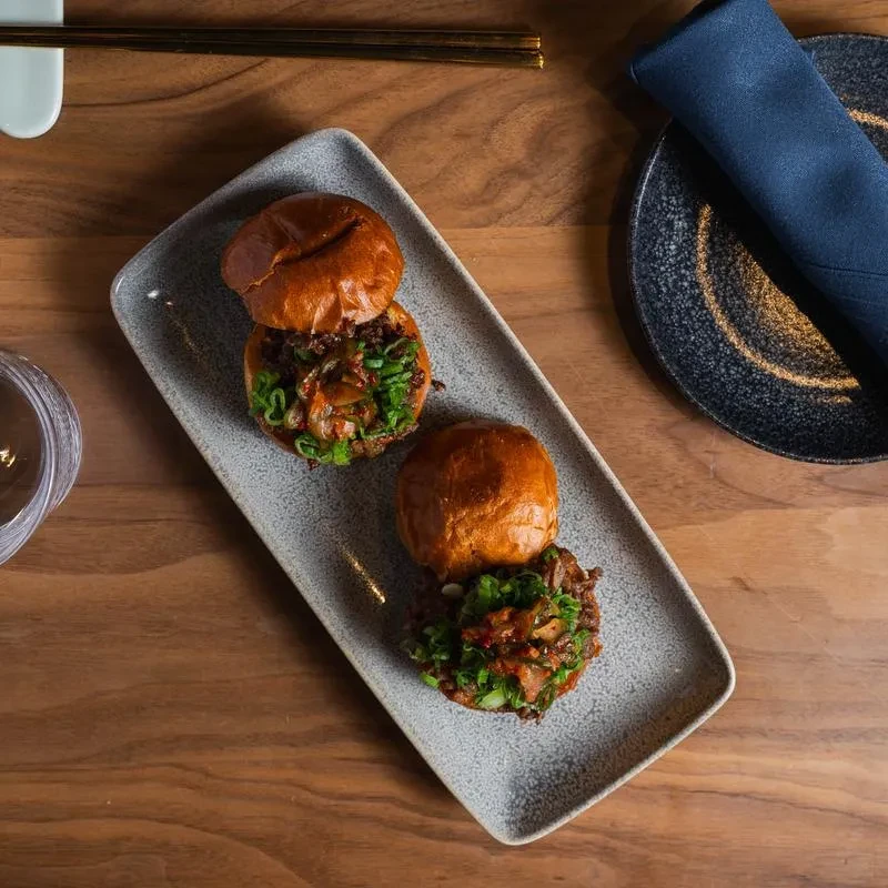 Overhead: two brioche sliders with meat, scallions, relish on a plate.