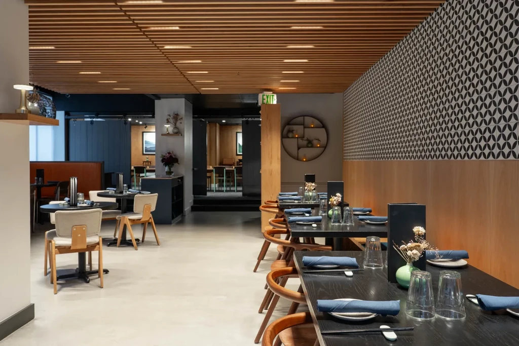 Modern restaurant interior with communal table, slatted ceiling, patterned wall.