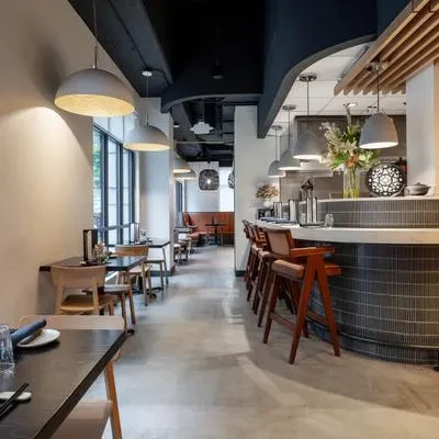 Modern restaurant interior with dining tables, curved bar, and pendant lights.