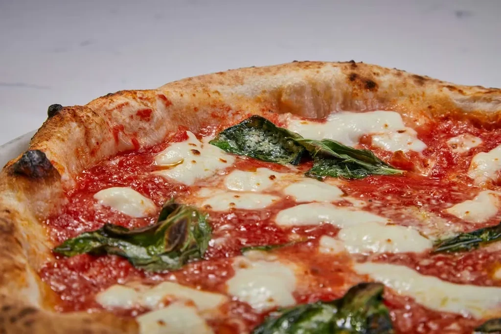 Neapolitan pizza: red sauce, mozzarella, basil, puffed, charred crust.