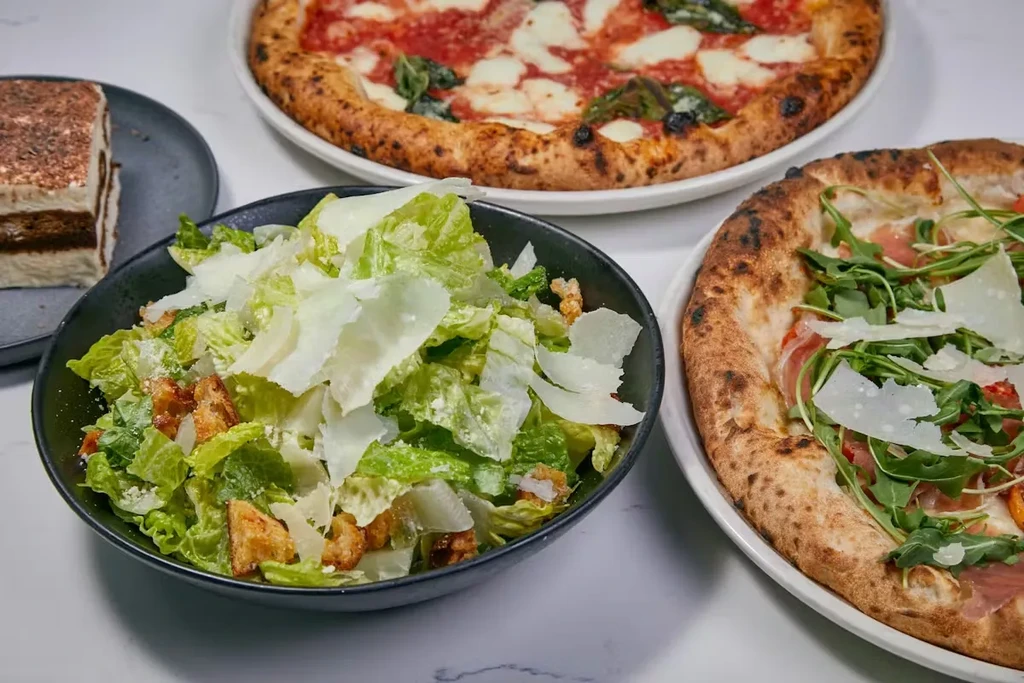Italian meal spread with Caesar salad, two pizzas, and tiramisu.