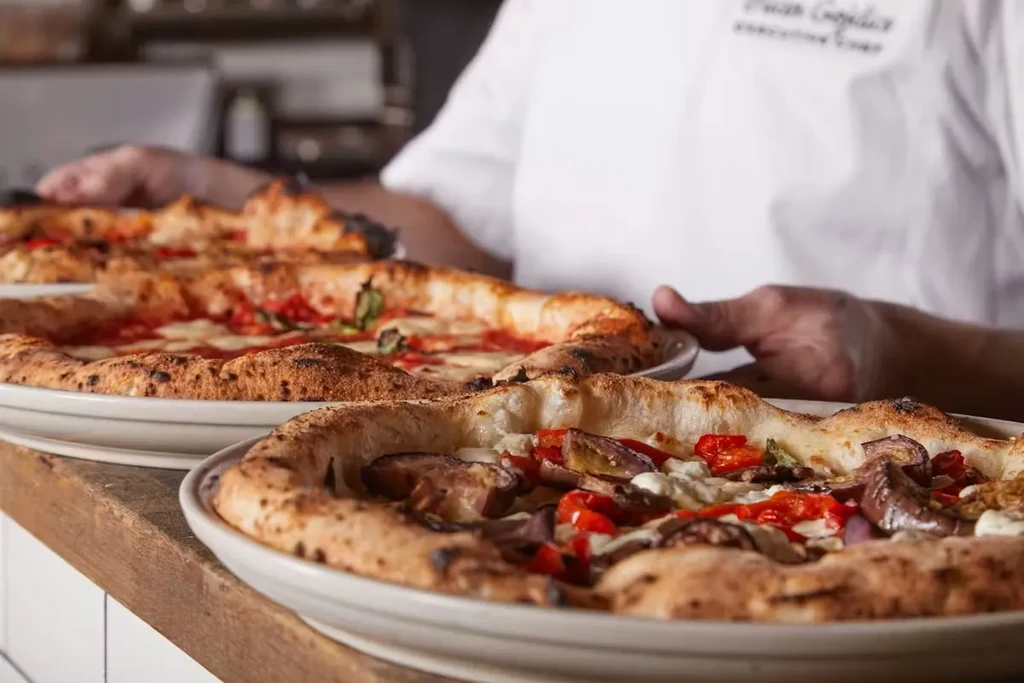 Chef serving multiple freshly baked pizzas on a rustic wooden counter.