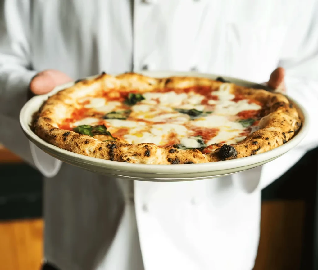 Chef holds close-up of fresh Neapolitan pizza with mozzarella, tomato, basil.