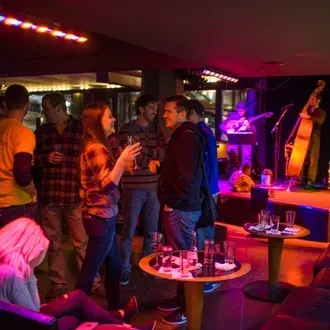 Colorful, dim bar: people socializing, musicians performing on stage.