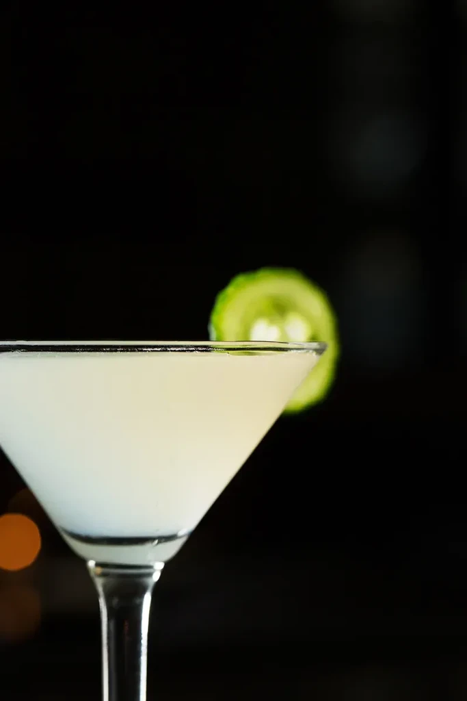 Elegant martini glass with pale cocktail and cucumber garnish.