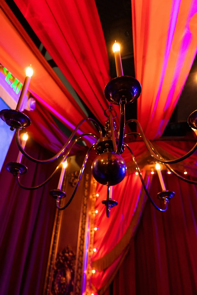 Ornate chandelier illuminates deep red and purple draped fabric.