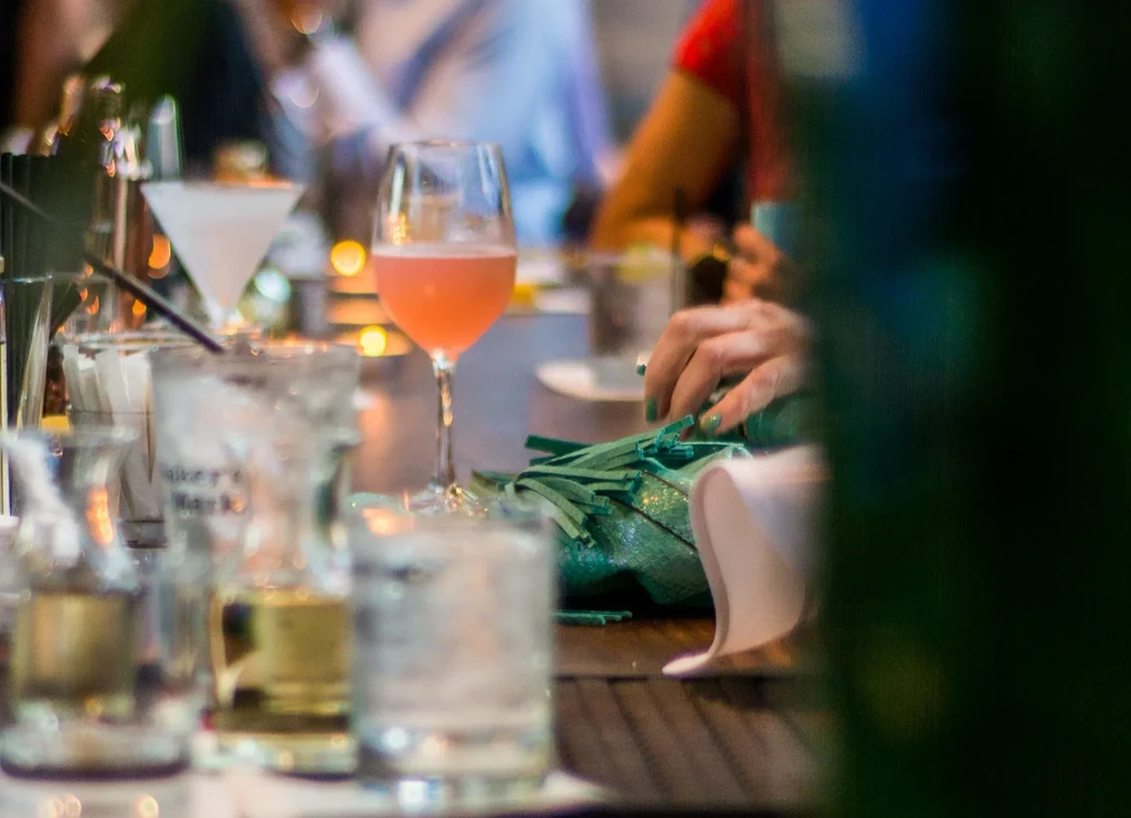 Pink cocktail and other drinks on a wooden bar table at evening.
