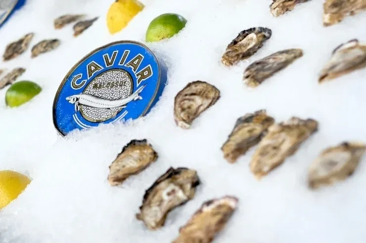 Shucked oysters, a blue caviar tin, and citrus wedges on crushed ice.