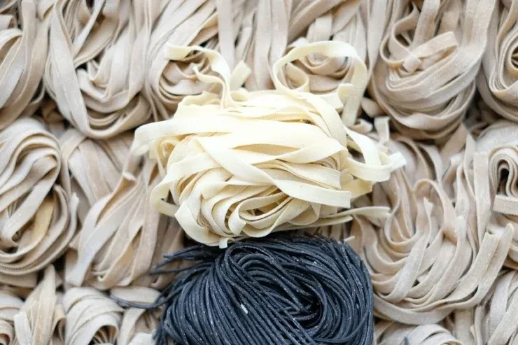 Raw fresh wide light noodles and contrasting thin dark pasta.