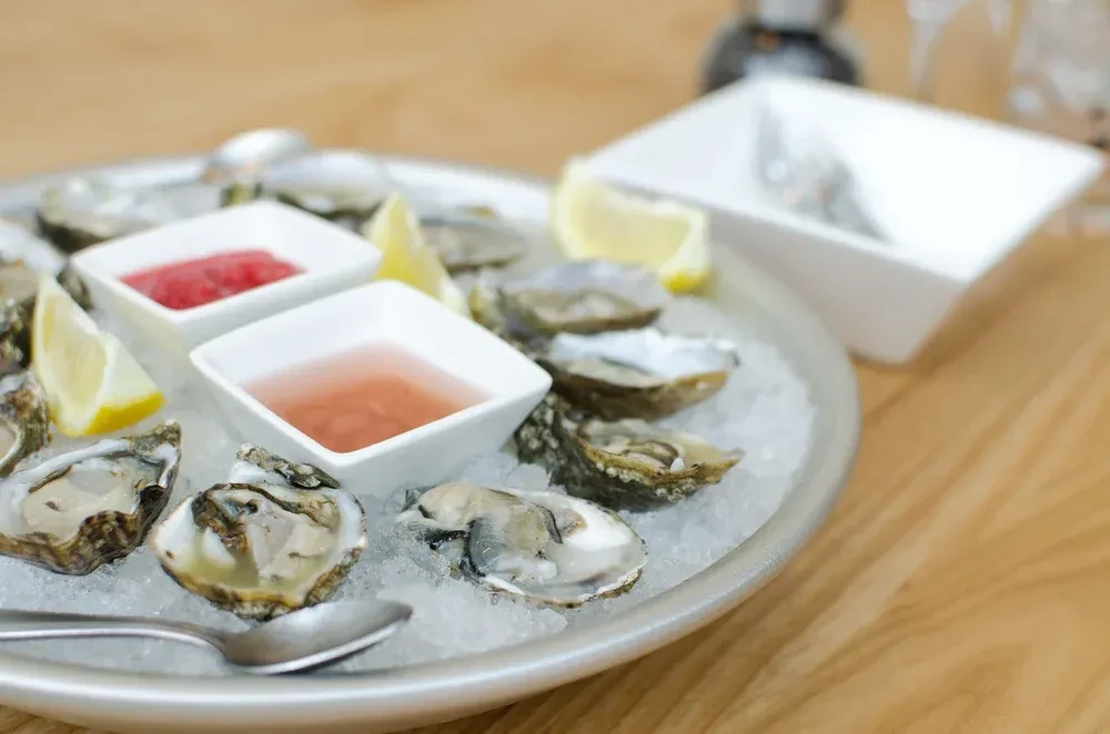 Platter of fresh oysters on ice with lemon wedges and sauces.