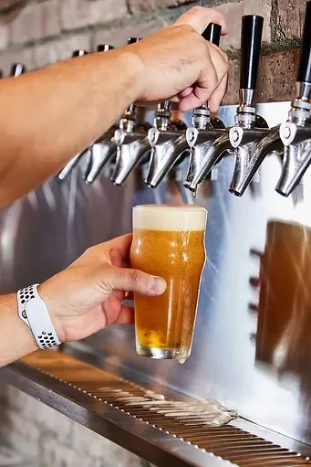 Hands pouring golden beer into a pint glass from a bar tap.