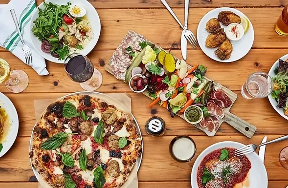 Flat lay of a wooden table with pizza, charcuterie, and beverages.