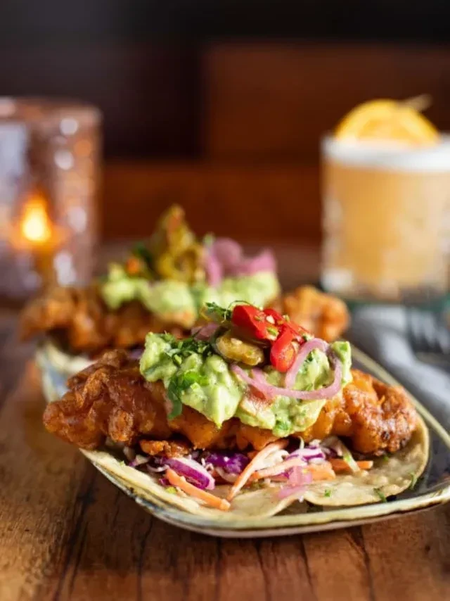 Two vibrant tacos with fried protein, slaw, guacamole, pickled onions.