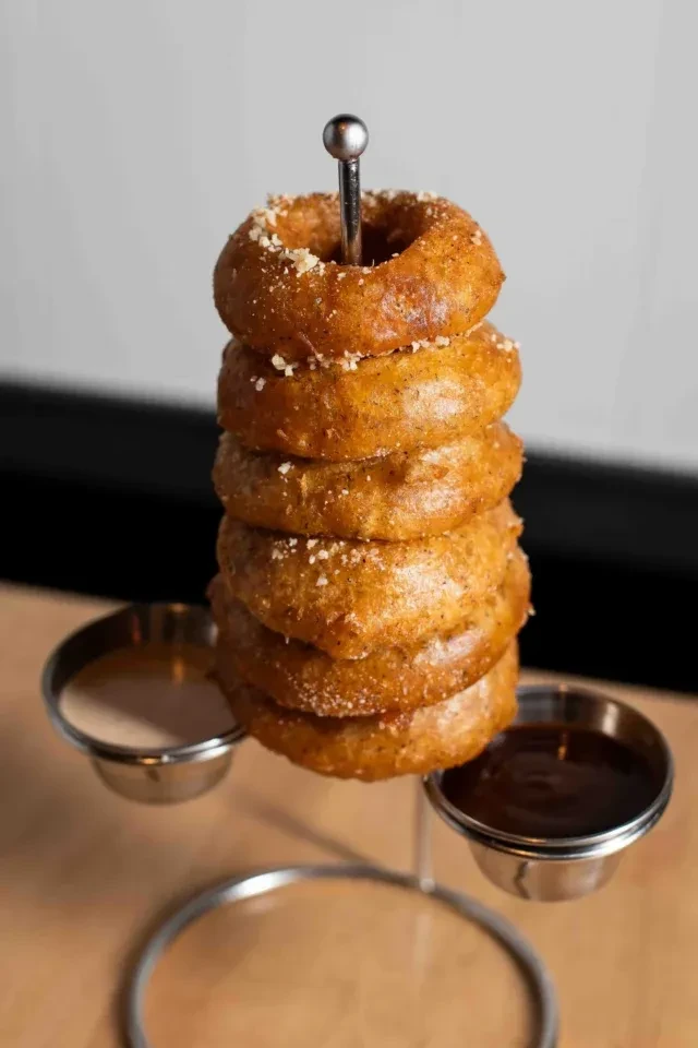 Golden-brown onion rings stacked on a stand with two sauces.
