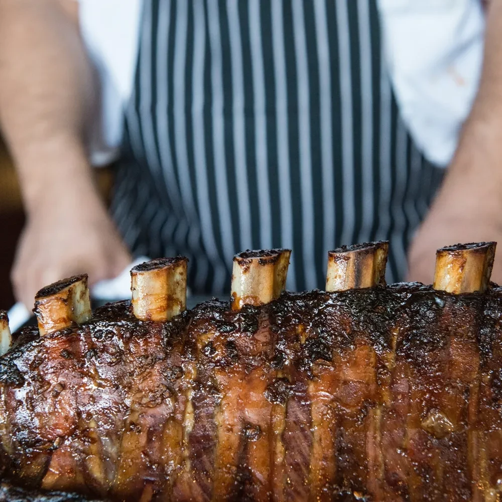 Close-up of glossy, bone-in roasted meat presented by a chef.