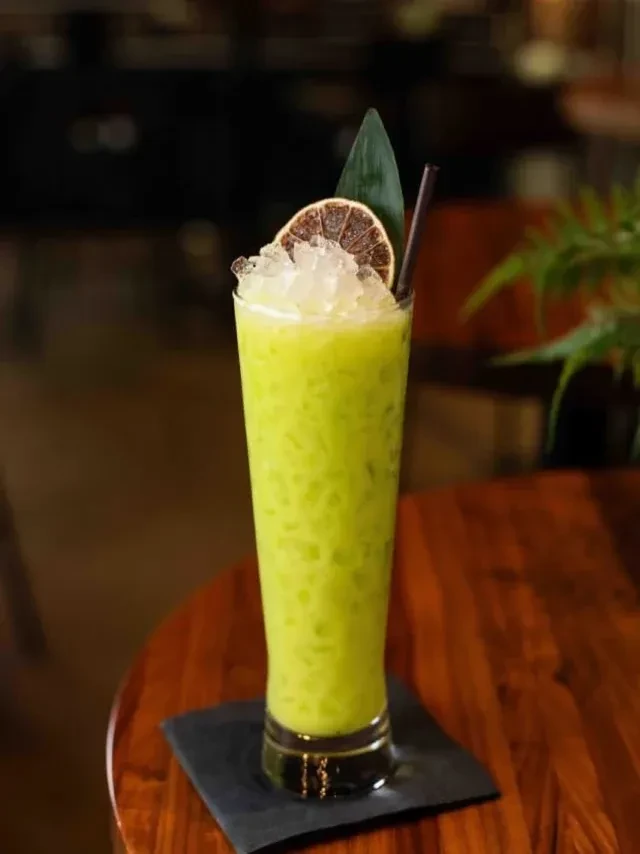 Light green beverage with crushed ice and citrus on a wooden table.