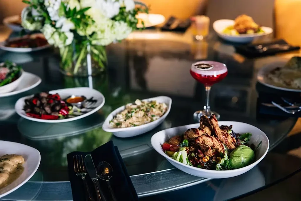 Restaurant table with a large salad, red cocktail, and floral centerpiece.