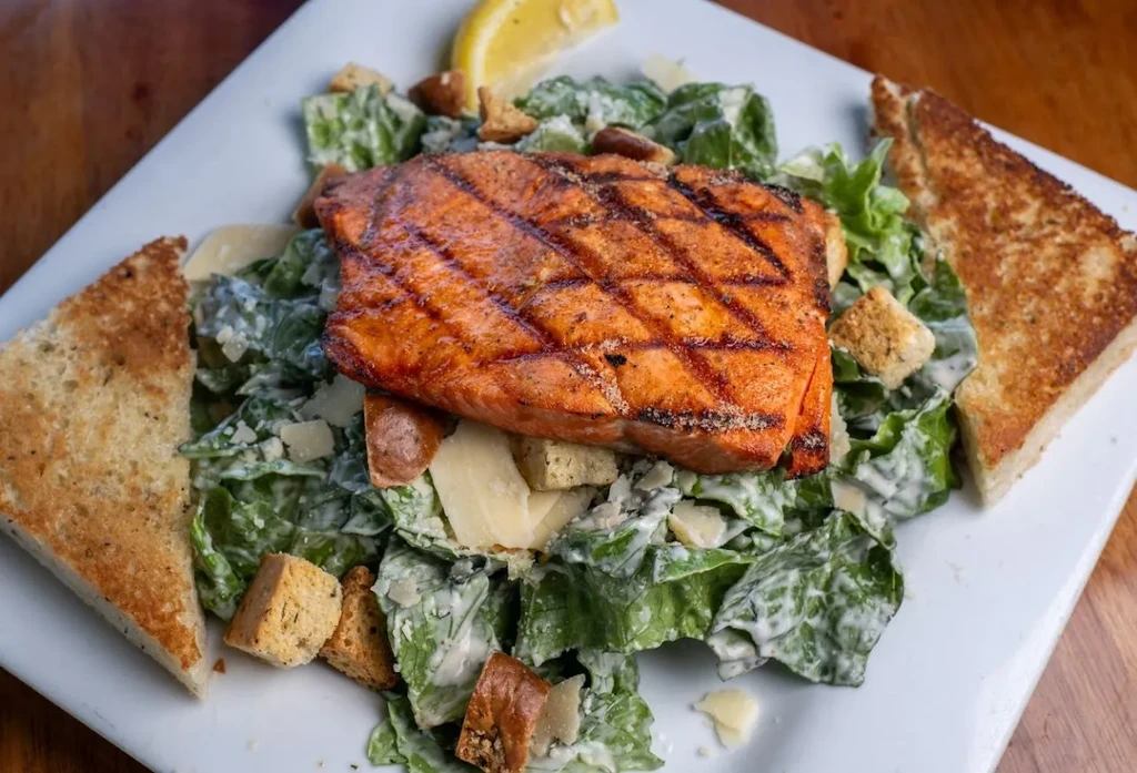 Close-up grilled salmon Caesar salad with lemon and bread.