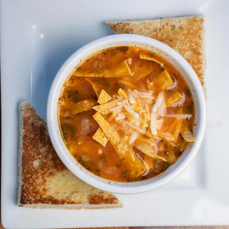 Reddish-orange tortilla soup with cheese, tortilla strips, and toasted bread.