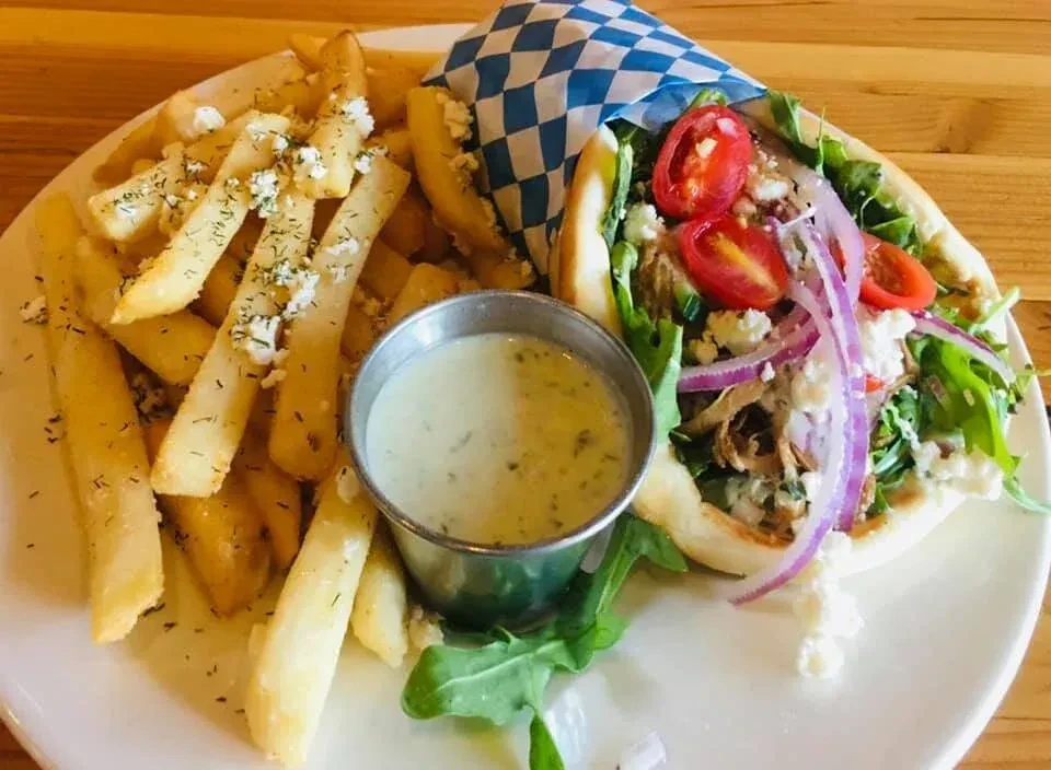 Plate with a pita wrap, feta-seasoned fries, and a green herb sauce.