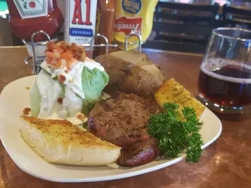 Steak, baked potato, side salad, garlic bread, and a dark beverage.