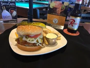 Burger with a pickle spear and knife, fries, sauce, and Rainier beer.