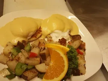 Two Eggs Benedict, hollandaise, breakfast potatoes, orange garnish.