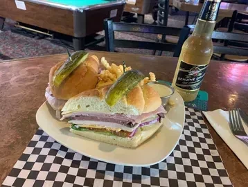 Sub sandwich with fries, pickles, beer on checkerboard placemat in a pub.