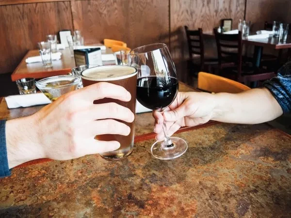 Hands clinking dark beer and red wine glasses on a restaurant table.
