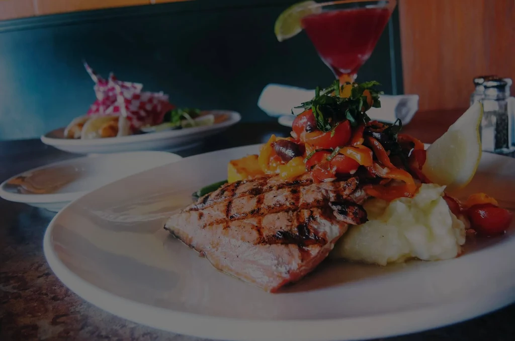 Grilled salmon with vegetables, mashed potatoes, and a drink in a restaurant.