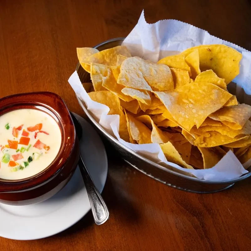 Queso dip with tomatoes and green onions, and tortilla chips.
