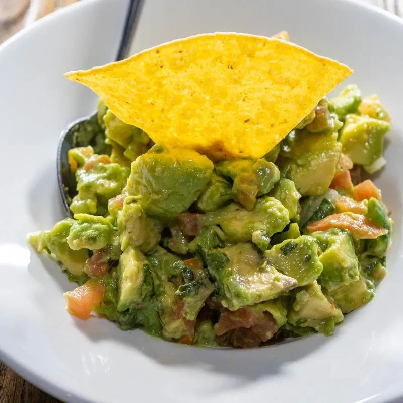 Chunky guacamole with a chip and spoon in a white bowl.