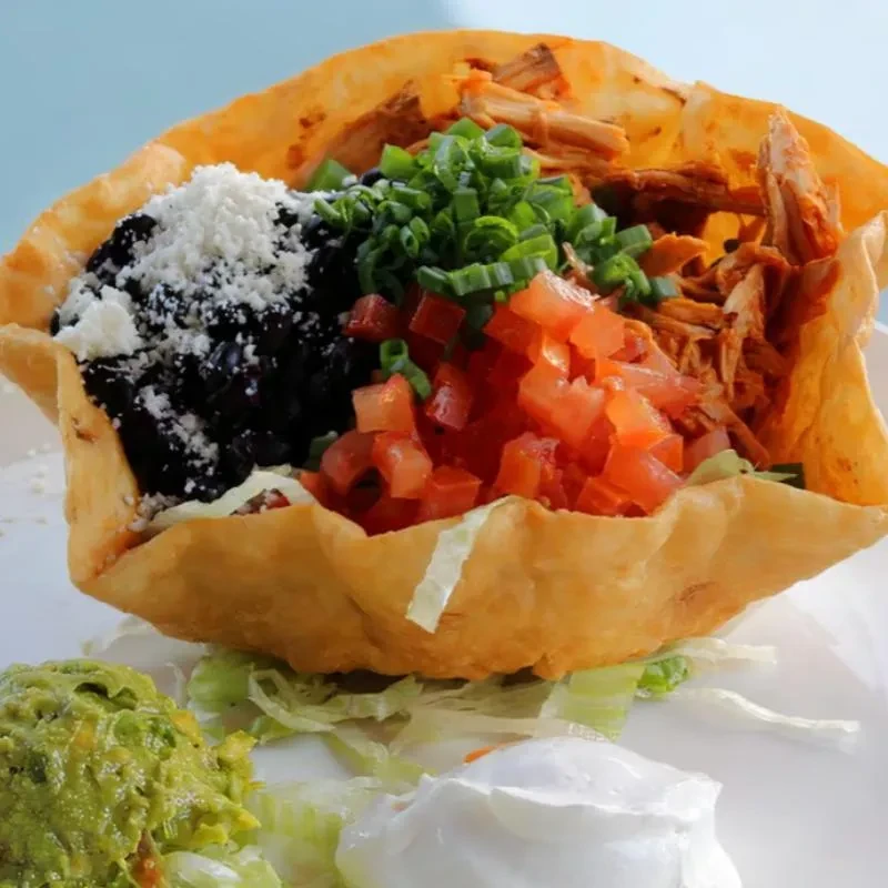 Fried tortilla bowl taco salad with meat, beans, cheese, guacamole, crema.