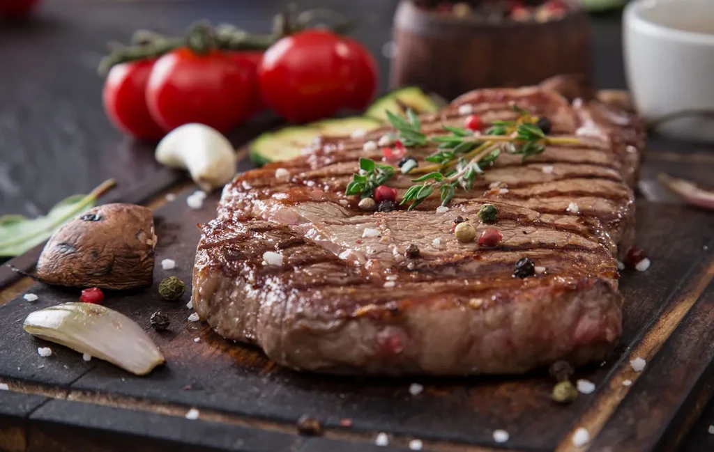 Seasoned grilled steak with fresh vegetables on a dark wooden board.