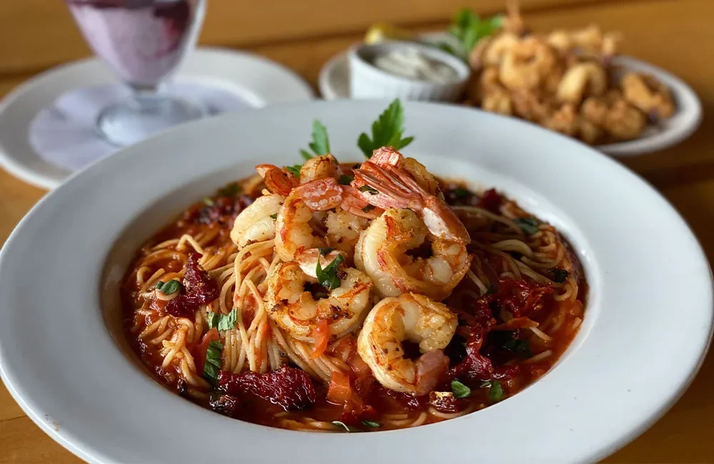 Plate of grilled shrimp pasta with red sauce, herbs, sun-dried tomatoes.
