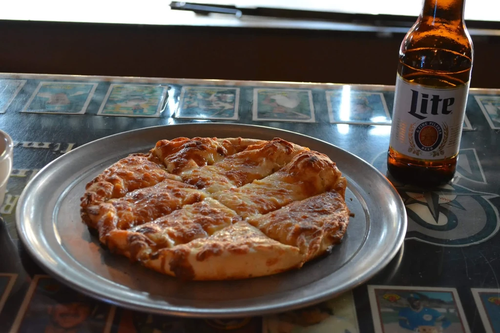 Melted cheesy pizza and Lite beer bottle on a Mariners table.