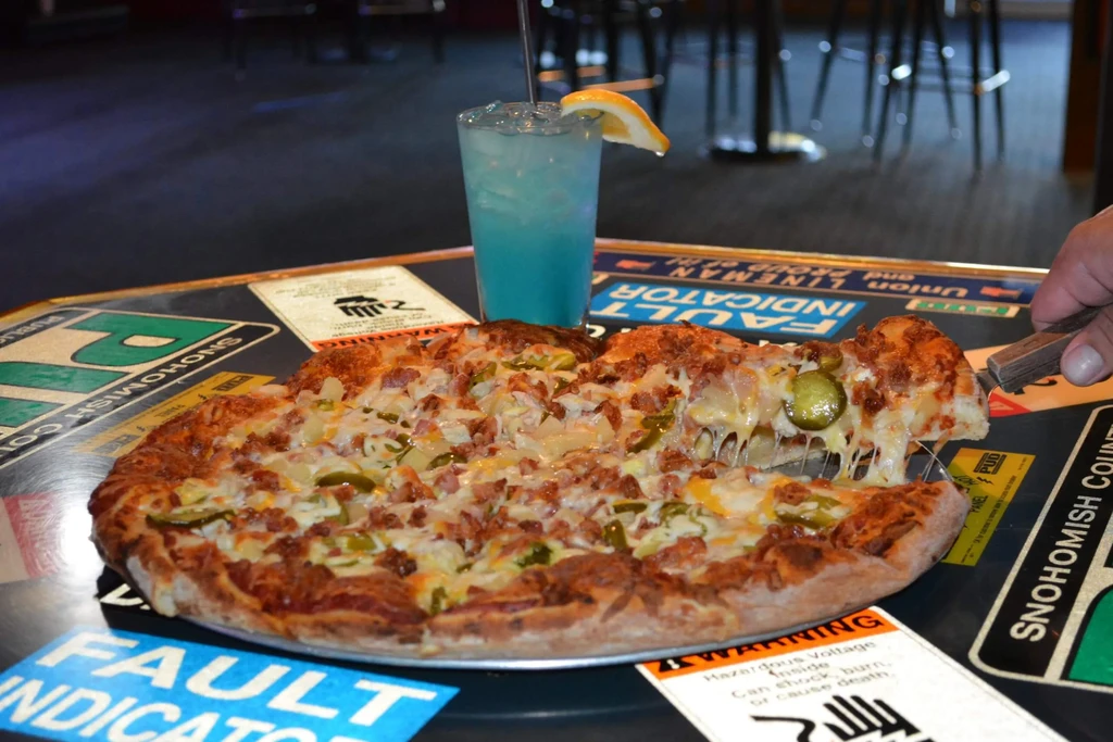 A hand lifts a pizza slice with meat, pickles, stretching cheese.