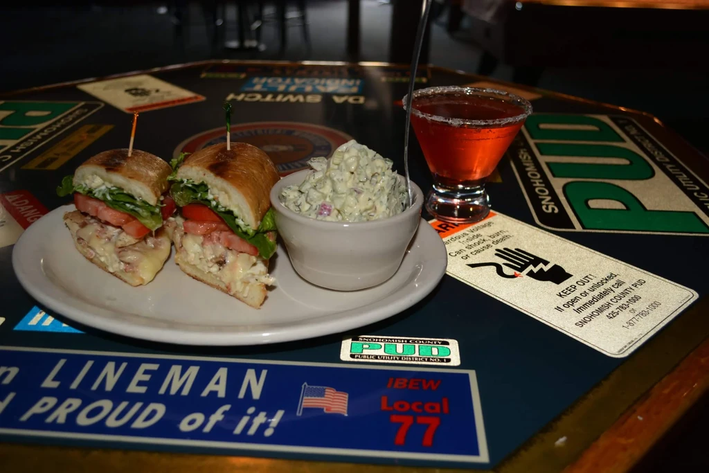 A sandwich, creamy salad, and cocktail on a decal-covered table.