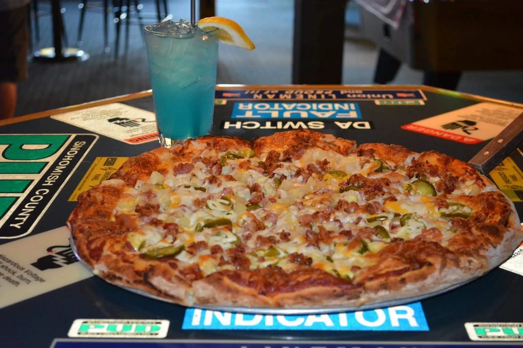 Large pizza with meat, pineapple, peppers, and a blue drink.