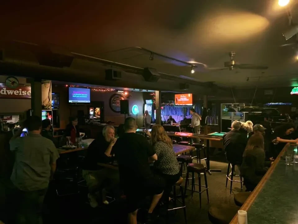 Dimly lit, lively bar interior with patrons, pool table, and karaoke.