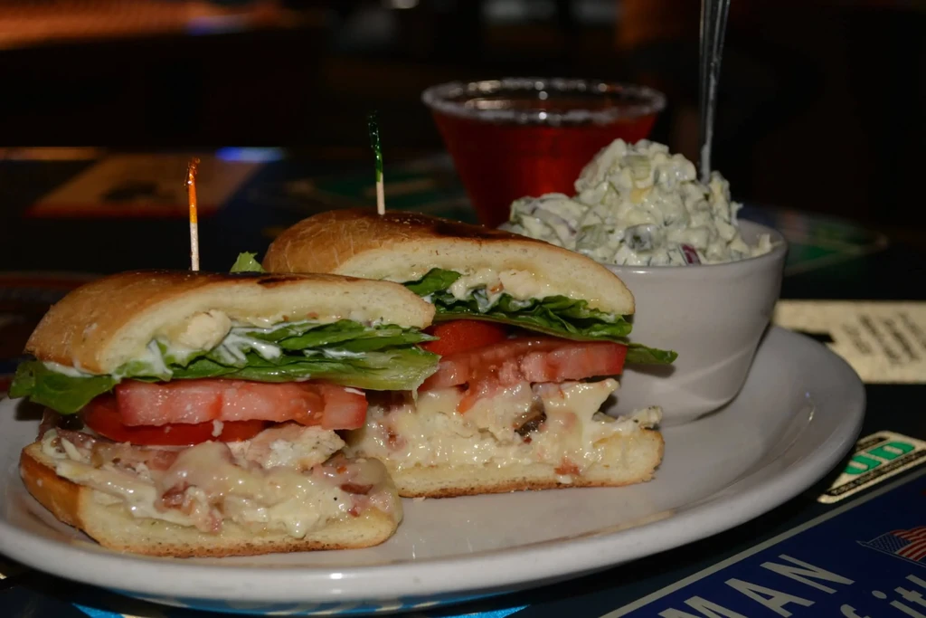 Close-up of a chicken club sandwich, coleslaw, and a red cocktail.