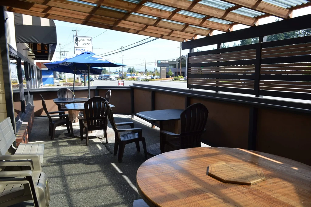 Empty, sunny restaurant patio with Adirondack chairs, tables, and umbrella.