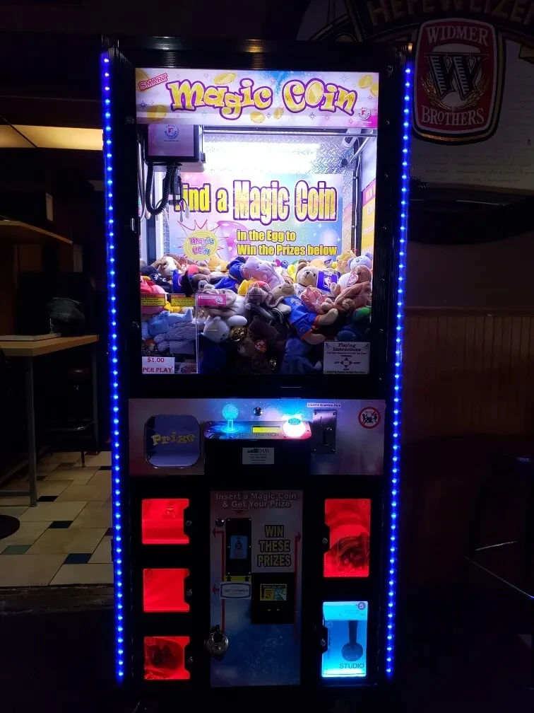 Brightly lit 'Magic Coin' claw machine in a dim restaurant bar.