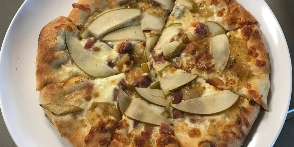 Round pizza topped with pear, meat, cheese, and caramelized onion.