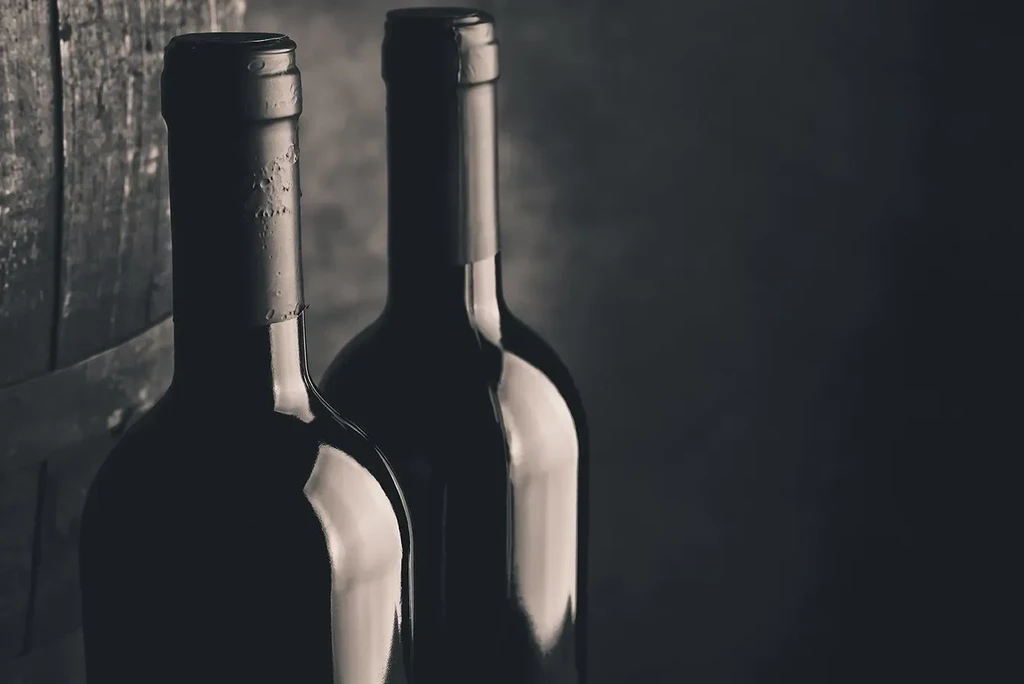 Close-up of two dark, sepia-toned wine bottles with rustic wood.