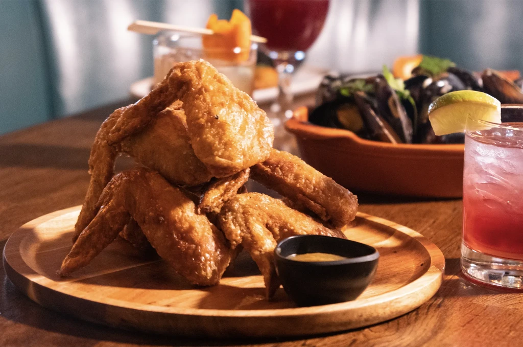 Golden-brown fried chicken wings on a wooden plate with dipping sauce.