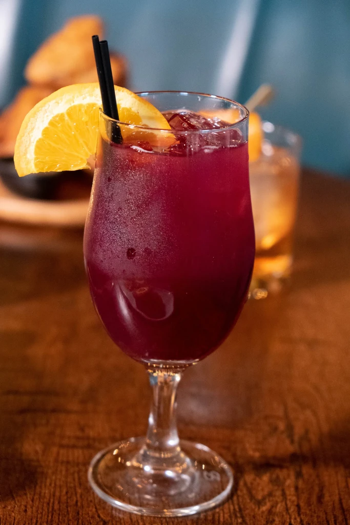 Dark red drink in frosted glass with orange and straws.