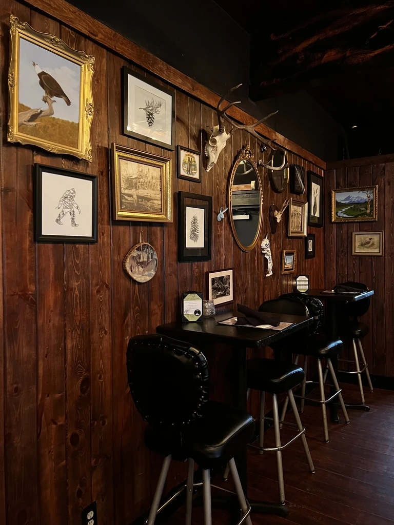 Rustic restaurant interior with wood walls, framed art, and high-top seating.