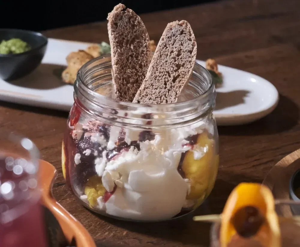 Layered cream and fruit dessert in a mason jar with biscotti.