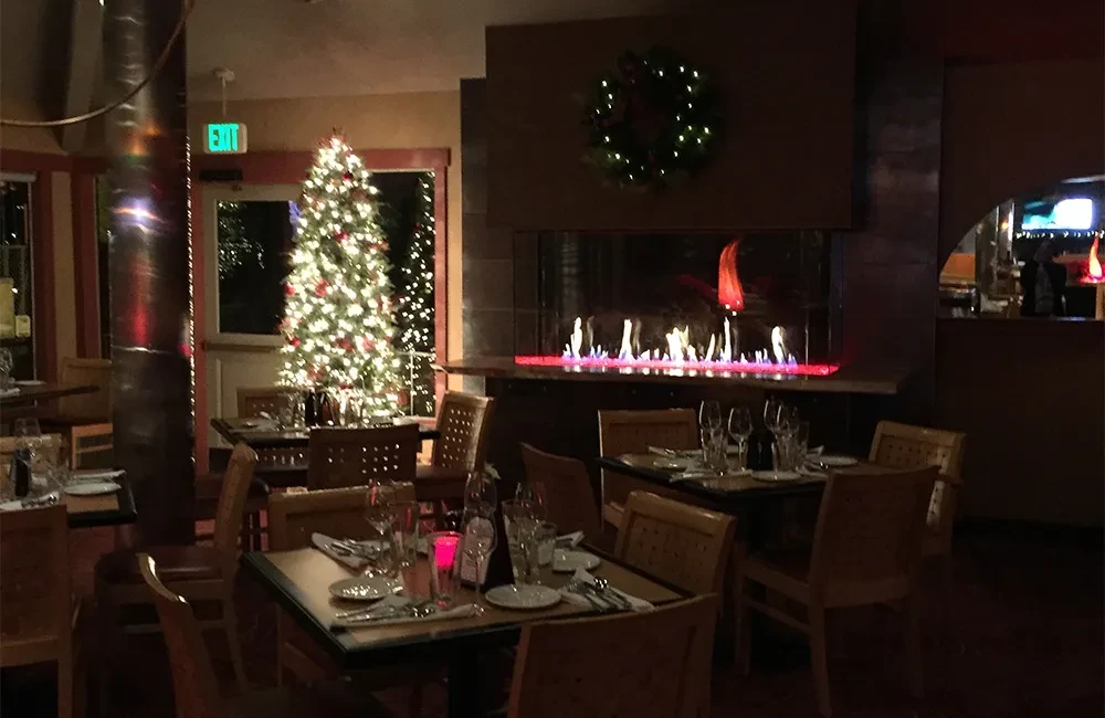 Holiday-decorated restaurant interior with fireplace, Christmas tree, and dining tables.